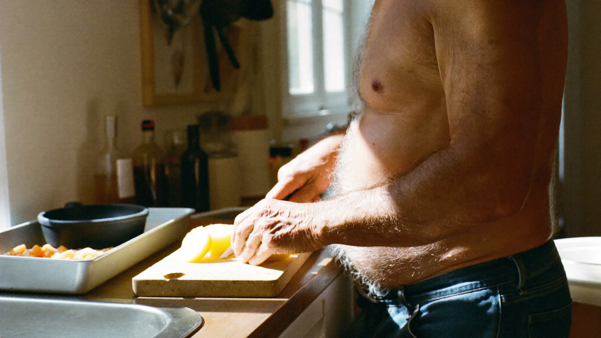 A man in his forties slicing fresh fruit and vegetables for breakfast in a sunlit kitchen